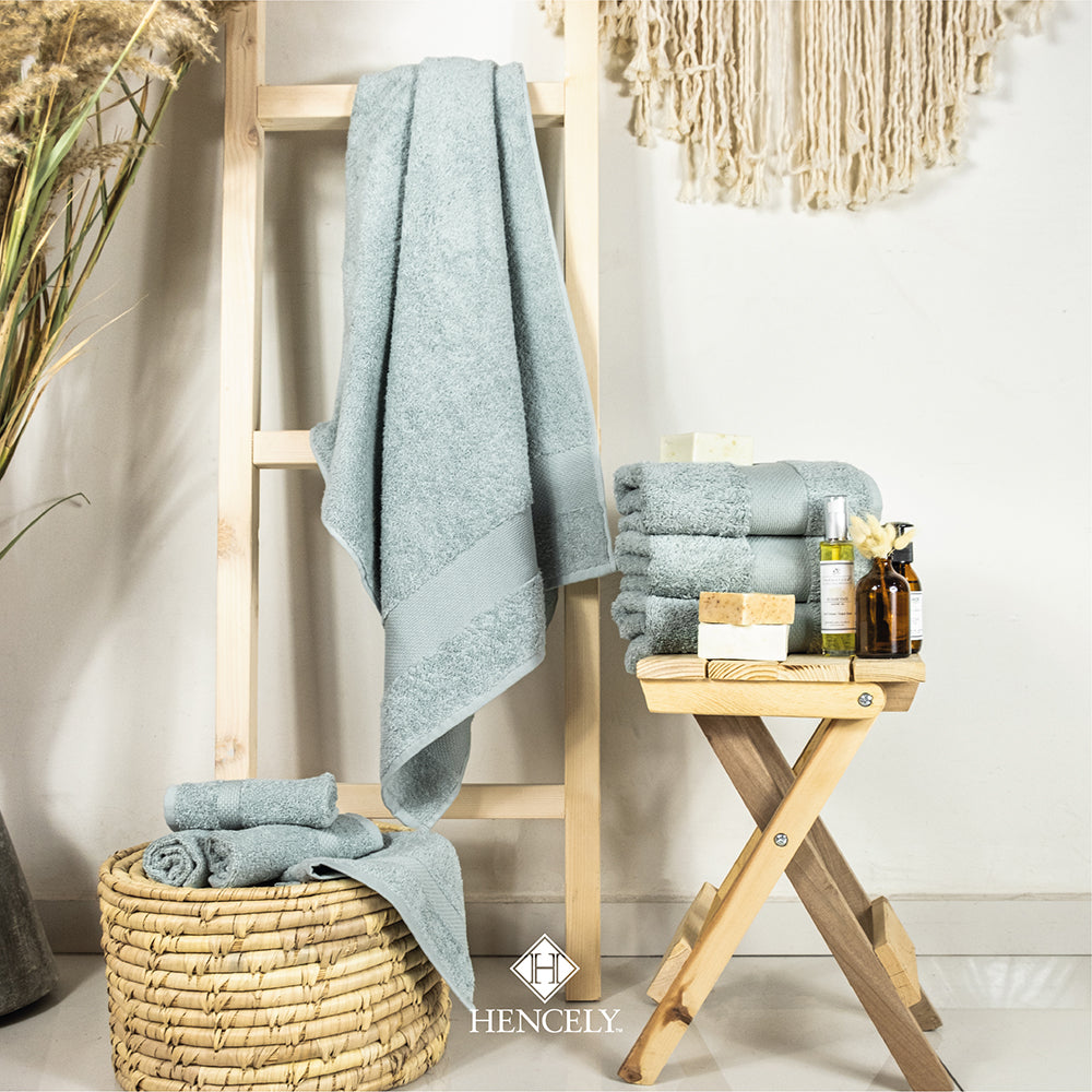 Stacked and hanging light green Turkish cotton bath sheets styled in a spa-inspired bathroom scene with wicker basket, wooden stand, and natural decor items.