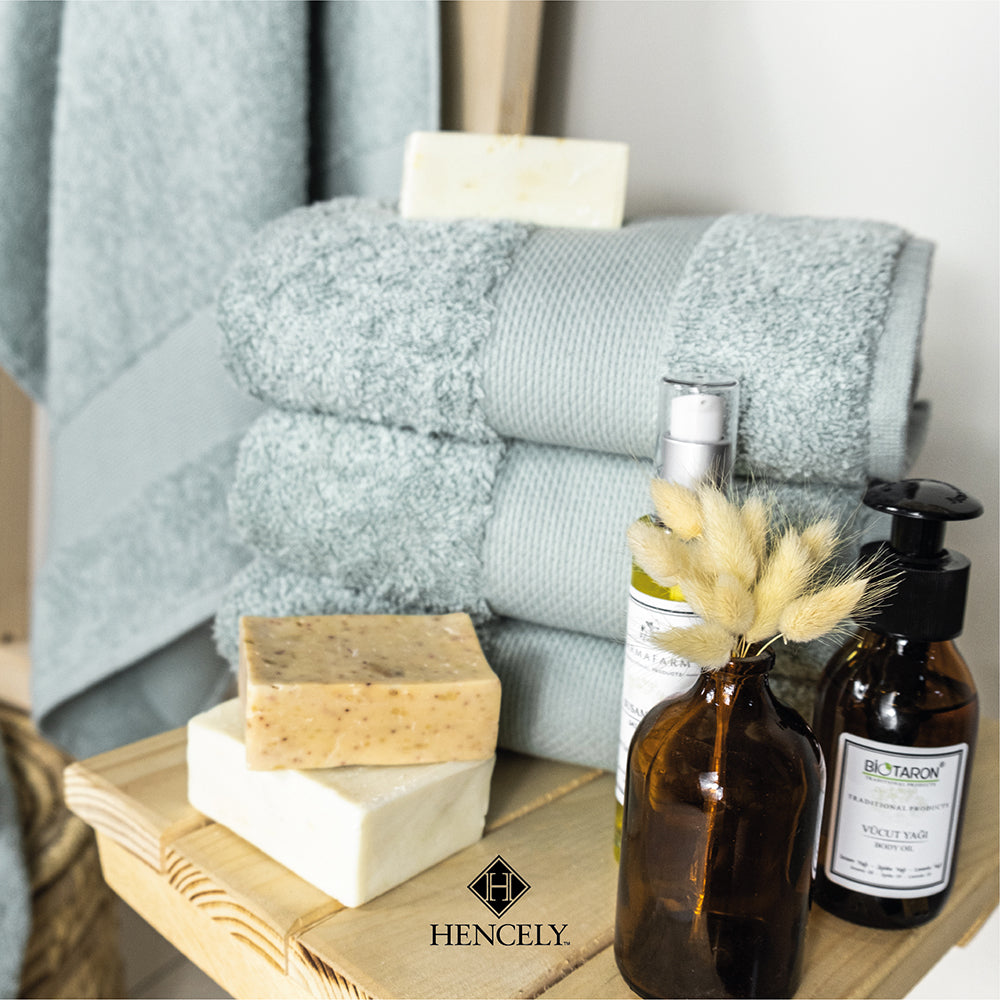 Folded light green Turkish cotton bath sheets stacked on a wooden stand, styled with natural soap bars, amber glass bottles, and dried floral decor for a spa-like ambiance.