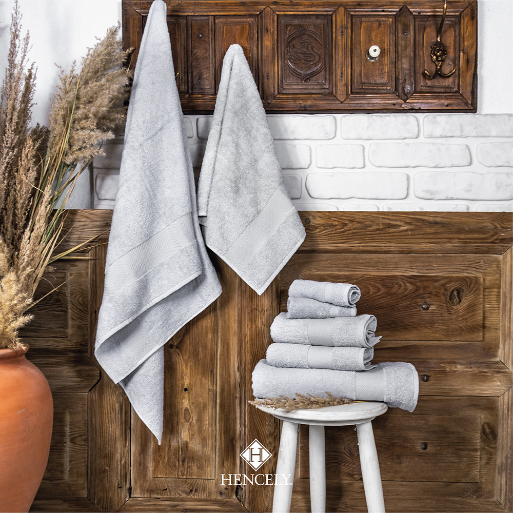Silver Turkish cotton bath sheet set displayed in a rustic bathroom setting with towels hanging and neatly folded on a stool.