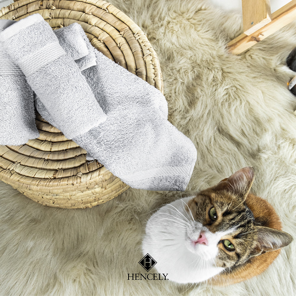 Silver cotton bath sheet set displayed on a woven basket with a cozy rug and a cat, creating a warm and homely atmosphere.