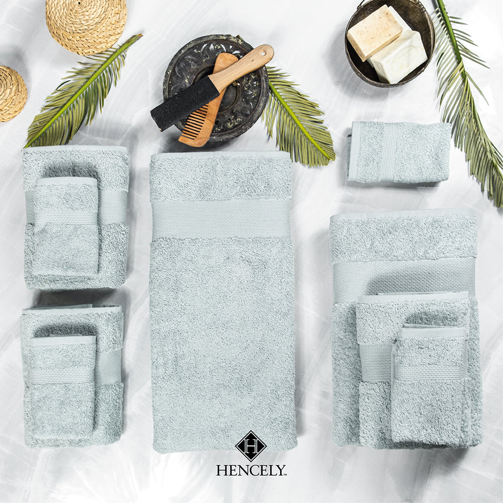 Light green Turkish cotton towel set arranged flat lay—bath sheet, hand towels, and washcloths—styled with palm leaves, soap bars, and a wooden comb on a marble background.