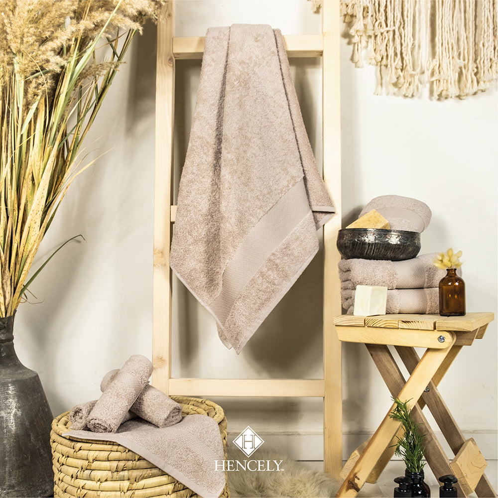 Beige Turkish cotton bath sheet displayed in a cozy bathroom setup with folded towels, a hanging towel on a wooden ladder, wicker basket, soaps, and decorative plants, styled by Hencely.
