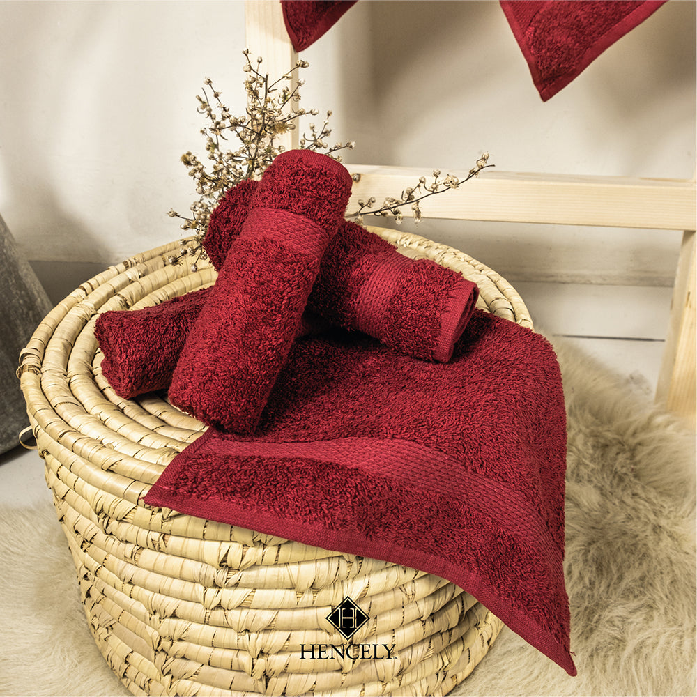 Burgundy Hencely bath sheets rolled and displayed on a woven basket with cozy spa-style decor