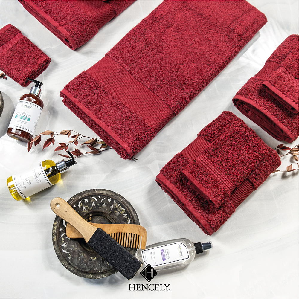 Burgundy Hencely bath sheet and towel set styled with bath oils, soap, and accessories on a marble background