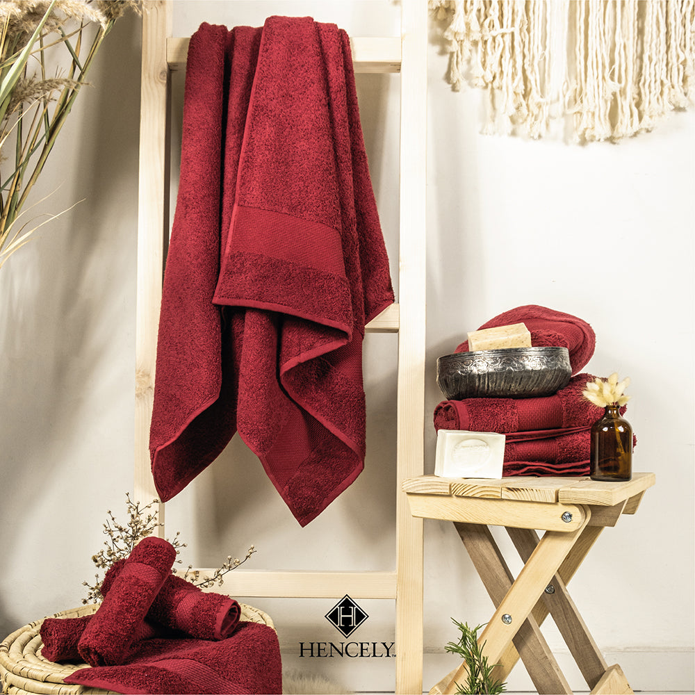 Burgundy Hencely bath sheets hanging on a wooden ladder with matching rolled towels, soap, and spa decor accessories