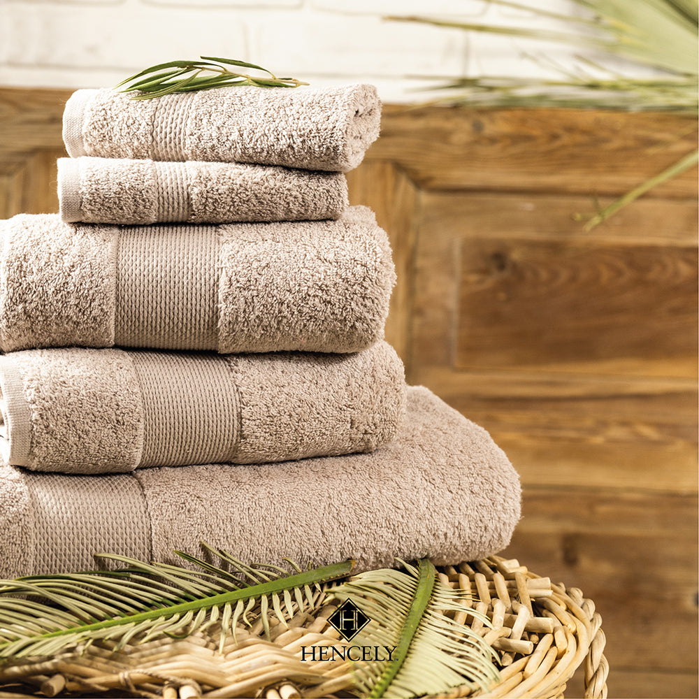 Stacked beige Turkish cotton bath sheets by Hencely on a wicker basket with rustic wooden background.