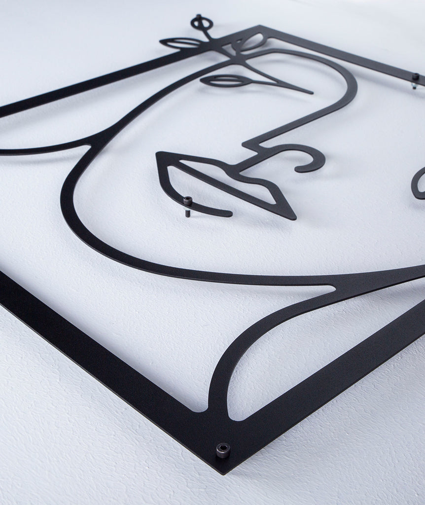 Angled close-up of black line art metal wall decor, highlighting the abstract female silhouette design with floral details.