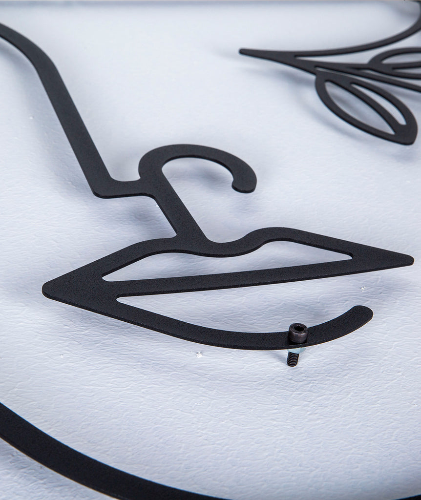 Close-up detail of black line art metal wall decor, showing the facial outline and lips of a female silhouette design with flowers.