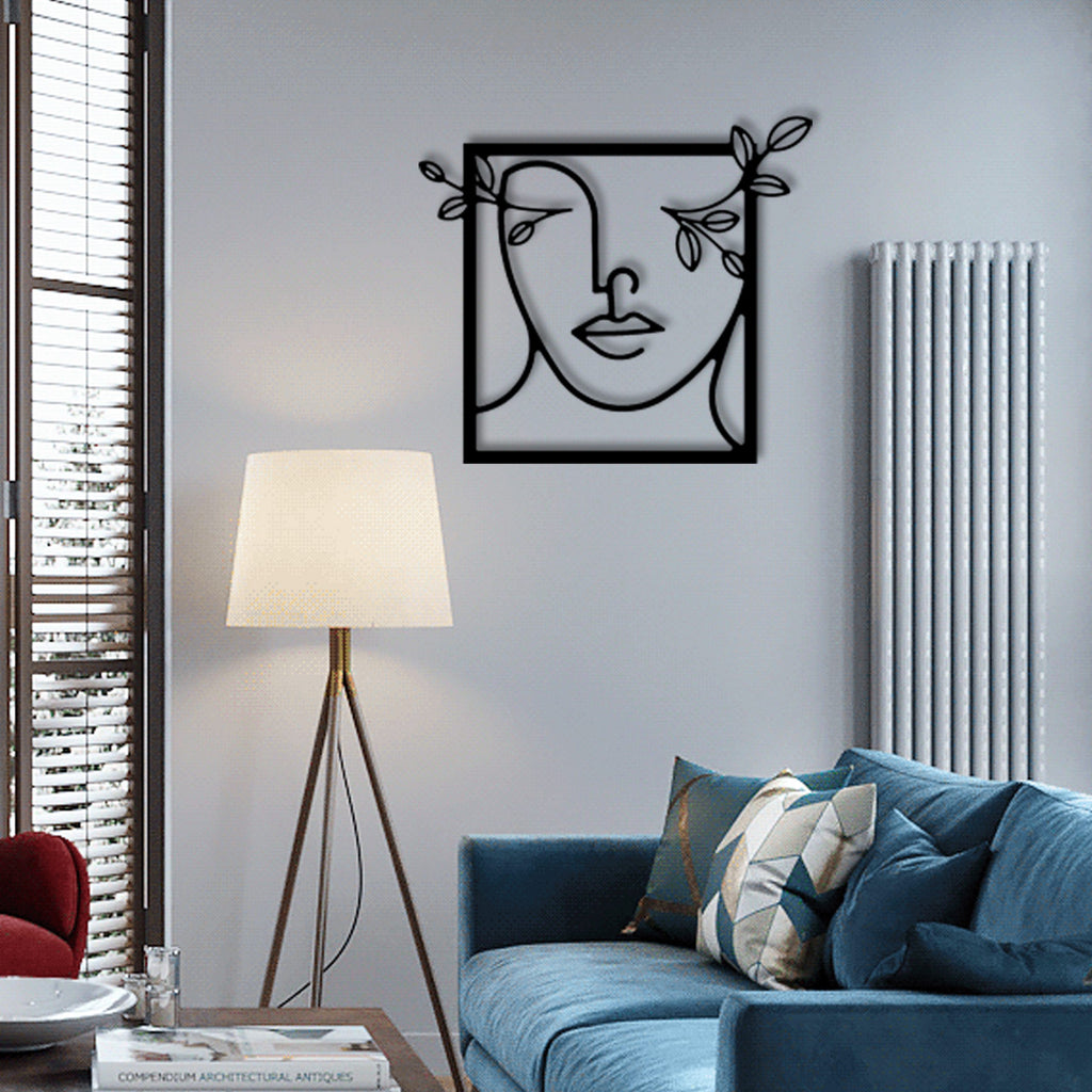 Black line art metal wall decor of a female silhouette with flowers, mounted on a light gray wall above a modern blue sofa and next to a floor lamp.