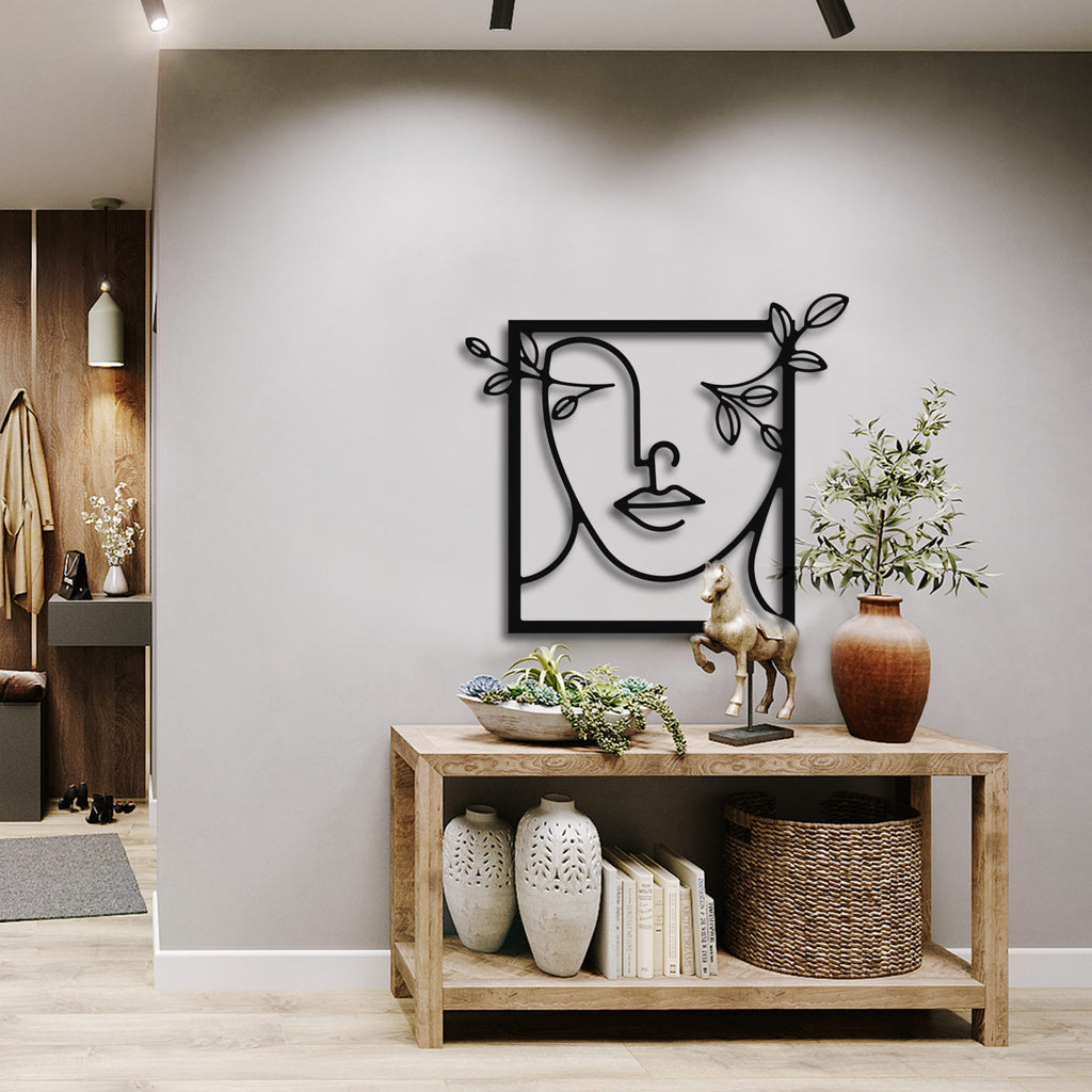 A black metal wall decor depicting a minimal line art woman with flowers, mounted on a wooden shelf in a room with various decor items.