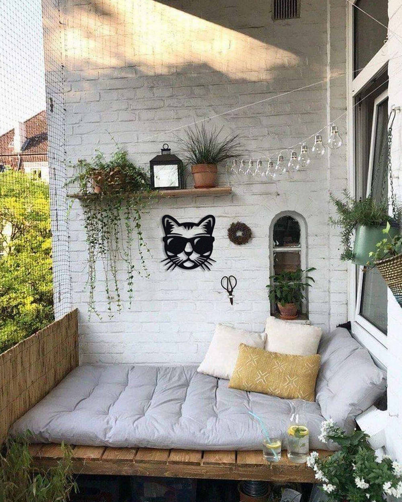 Black cat silhouette metal wall art in matte steel, displayed on a white brick balcony wall with plants, a cozy bench, and decorative pillows.