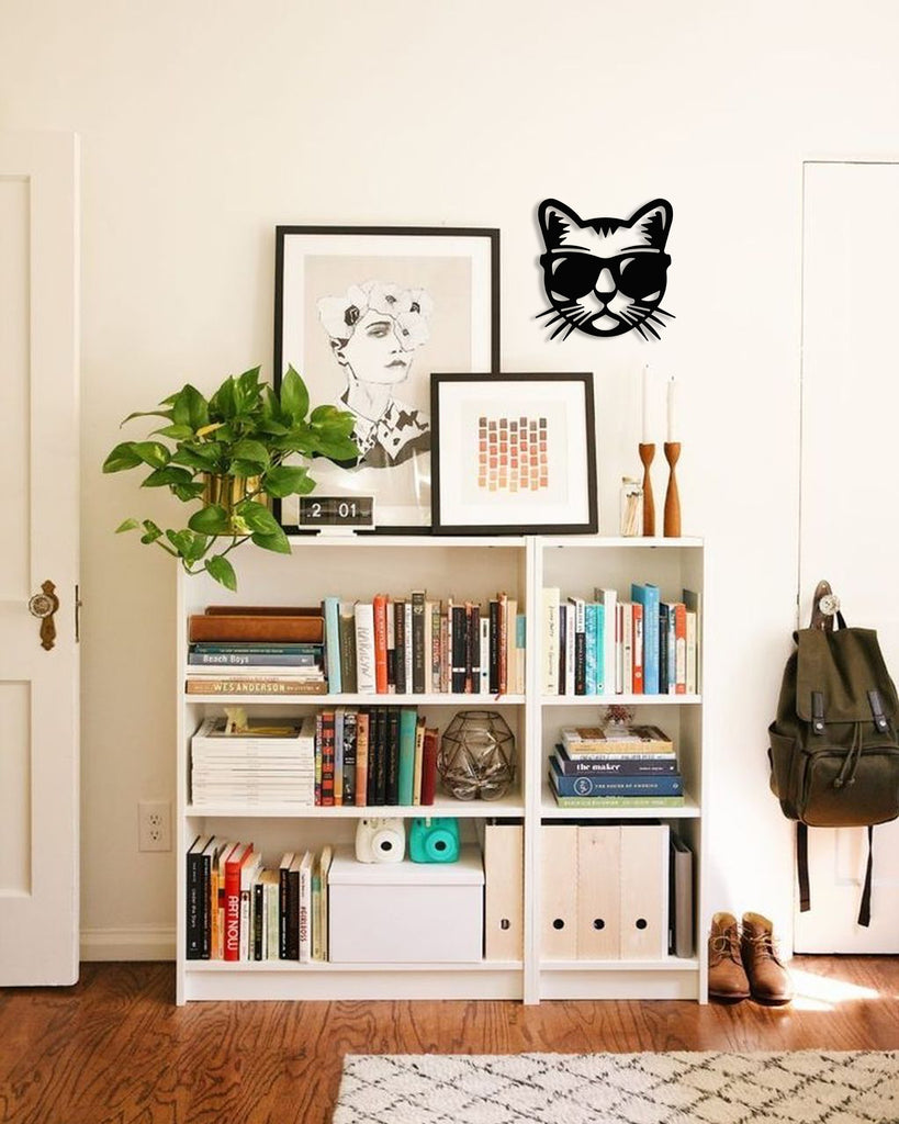 Black cat silhouette metal wall art in matte steel, mounted on a white wall above a bookshelf with framed art and indoor plants.