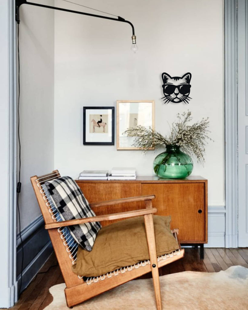 Black cat silhouette metal wall art in matte steel, displayed on a white wall above a wooden sideboard with a green vase and modern accent chair.