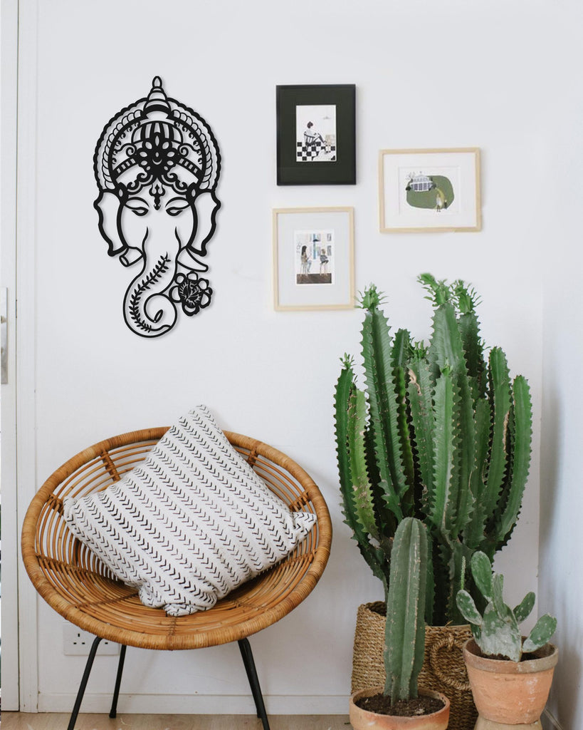 Black metal wall art depicting a Hindu god, Ganesh, with a decorative background including a potted plant and framed pictures.