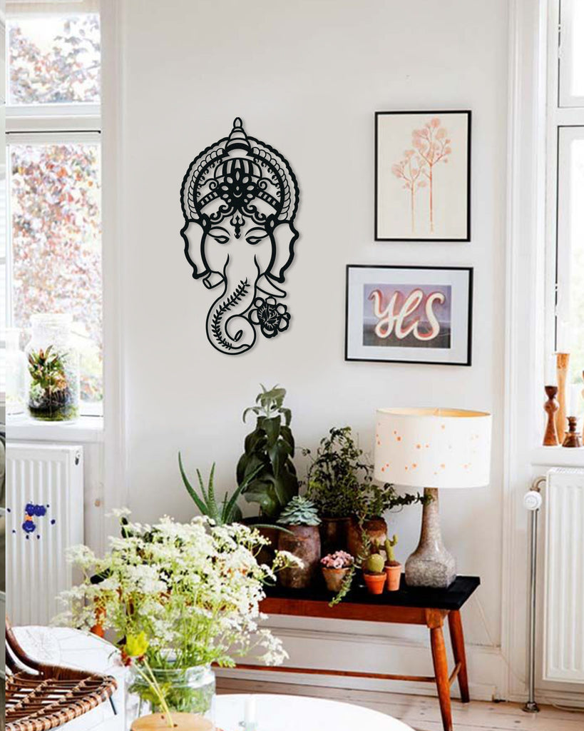 Black steel Ganesh metal wall art mounted on a white wall in a cozy living room with indoor plants, framed art, and a table lamp.