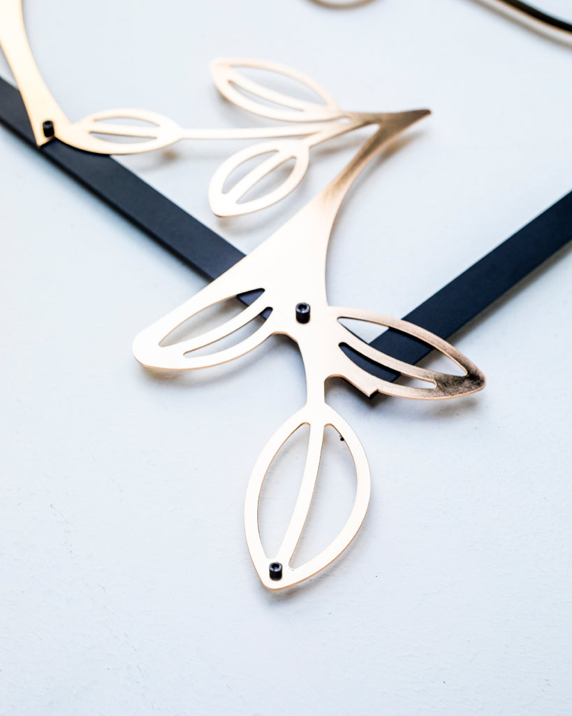 Close-up detail of gold line art metal wall decor showing floral elements of the female silhouette design with black steel frame.